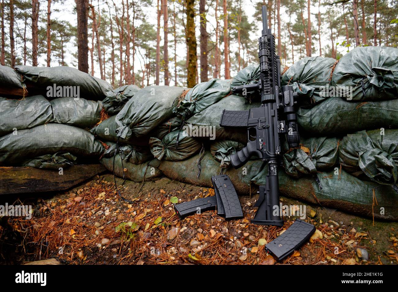 Airsoft replica M4-M16 leans on sandbags surrounding a foxhole. Stock Photo