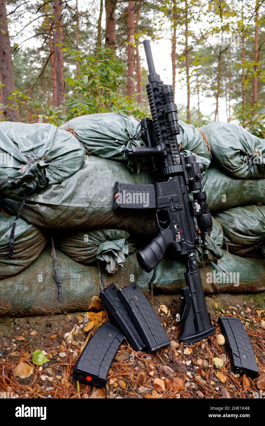 Airsoft replica M4-M16 leans on sandbags surrounding a foxhole. Stock Photo
