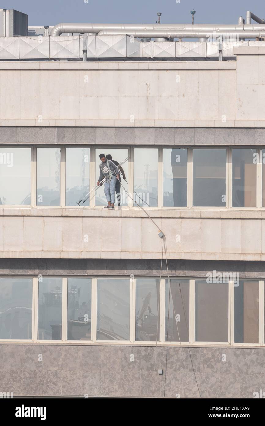 A window washer in Cairo, Egypt works at cleaning the glass of a high-rise building many floors up. Dangerous work with minimum safety equipment. Stock Photo