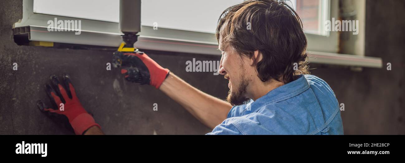 Man in a blue shirt does window installation BANNER, LONG FORMAT Stock Photo