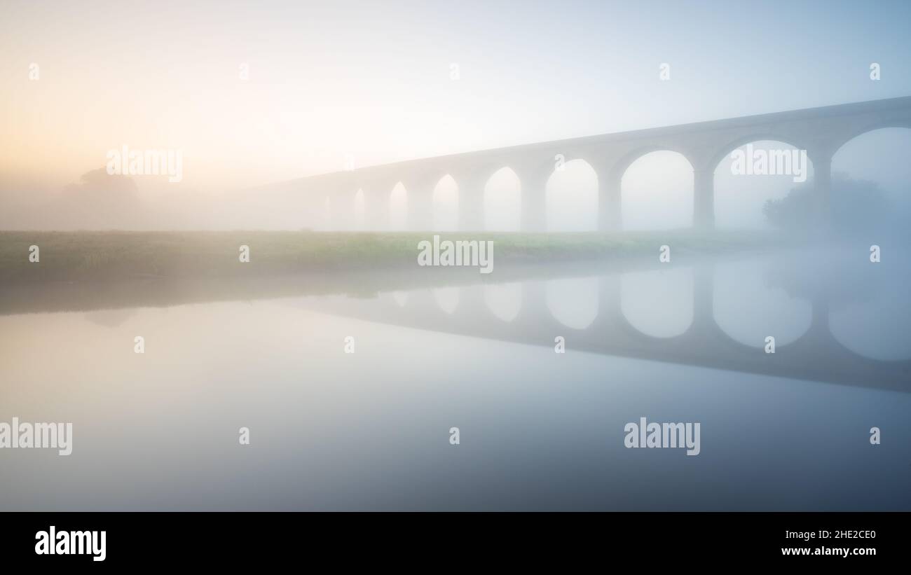 Soft diffuse sunrise light causes the drifting fog enveloping Arthington Viaduct to glow on a late spring morning in Lower Wharfedale. Stock Photo