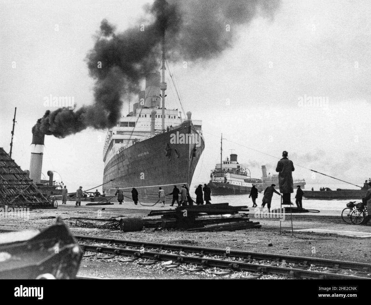 RMS Aquitania at Southampton docks, England, UK in the late 1940s. Aquitania was a British ocean liner of the Cunard Line. She built by John Brown & Company in Clydebank, Scotland. She was launched in 1913 and sailed on her maiden voyage from Liverpool to New York on 30 May 1914. She was used as a troop transport and a hospital ship in World War I. During World War II she served as a troop transport. After the war she transported migrants to Canada. Aquitania was retired from service in 1949 and was sold for scrapping the following year – a vintage 1940s photograph. Stock Photo