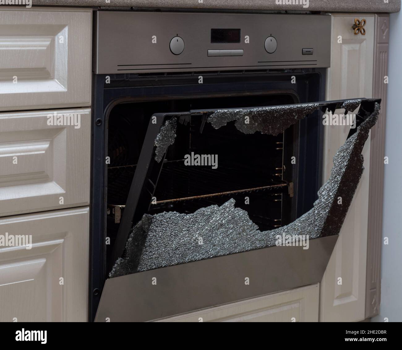 Opened broken oven door in the kitchen, side view, closeup. Broken glass from overheating
