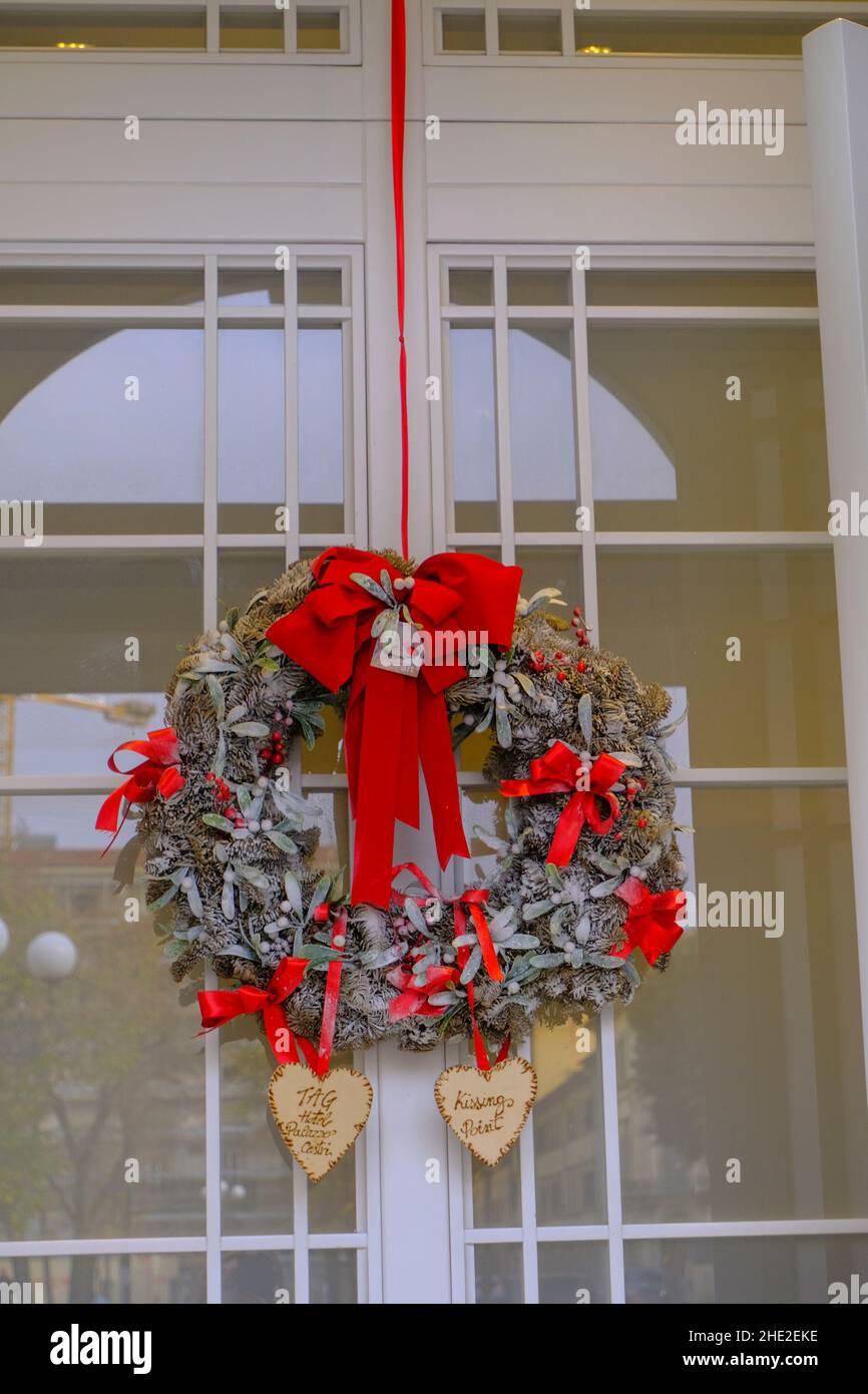 Christmas wreath with red bowls hanging on the white door close-up. Christmas outdoor decoration Stock Photo