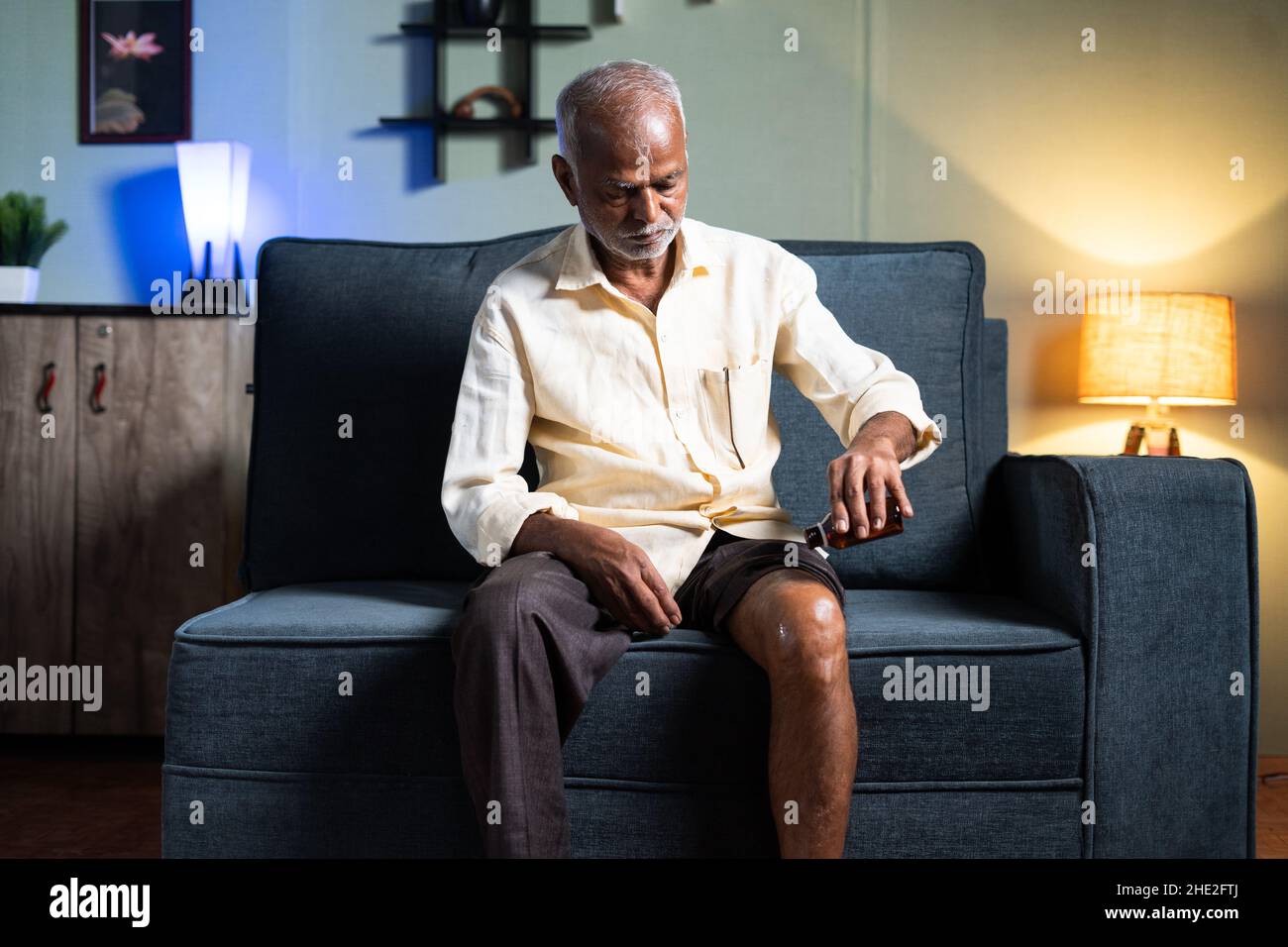 Old man using ayurvedic oil massage for knee joint paint at home on