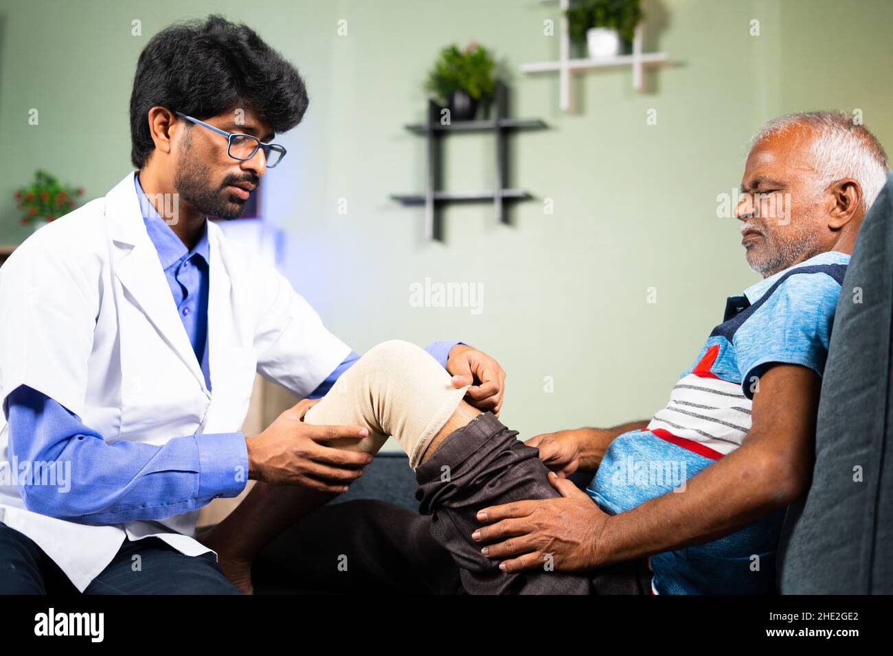 Orthopedic Physician treating or helping old man to wear knee support braces at home - concept of arthritis, spraintreatment and Doctor consultation Stock Photo
