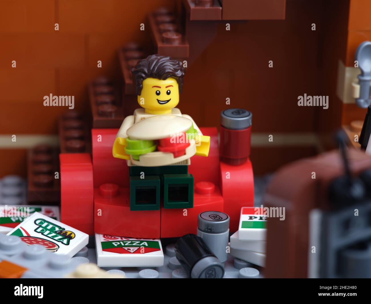 Tambov, Russian Federation - January 03, 2022 A Lego man sitting on a red couch eating a burger with pizza and soda cans near him Stock Photo