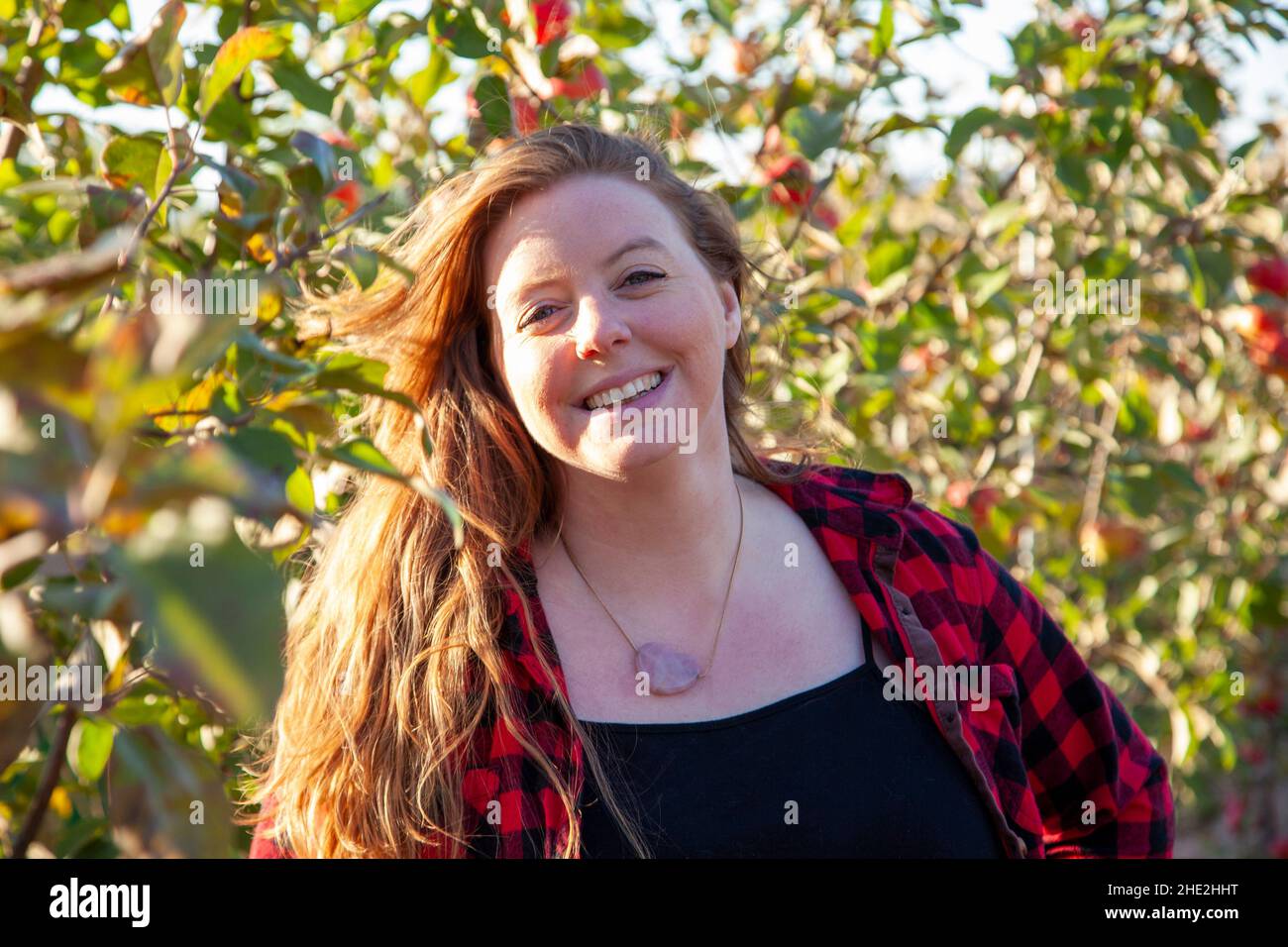 beautiful woman with a lovely smile and red hair grins in her apple orchard Stock Photo