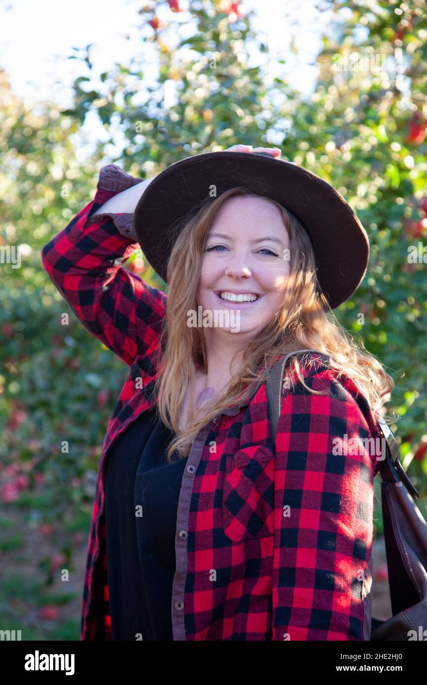beautiful relaxed woman in plaid and a hat explores the world in an apple orchard Stock Photo