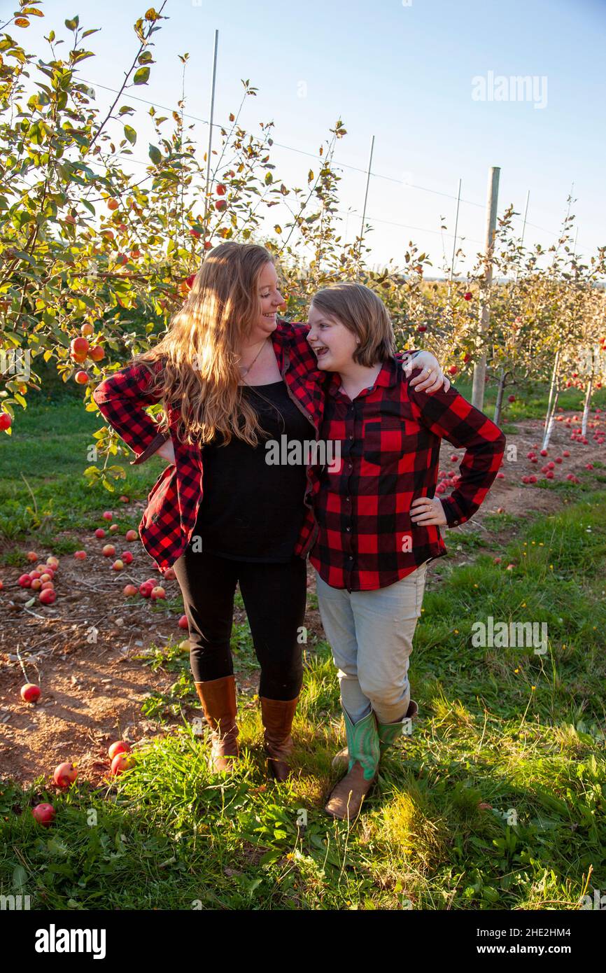 a redhaired mom and her child laugh and stand together in their apple orchard Stock Photo
