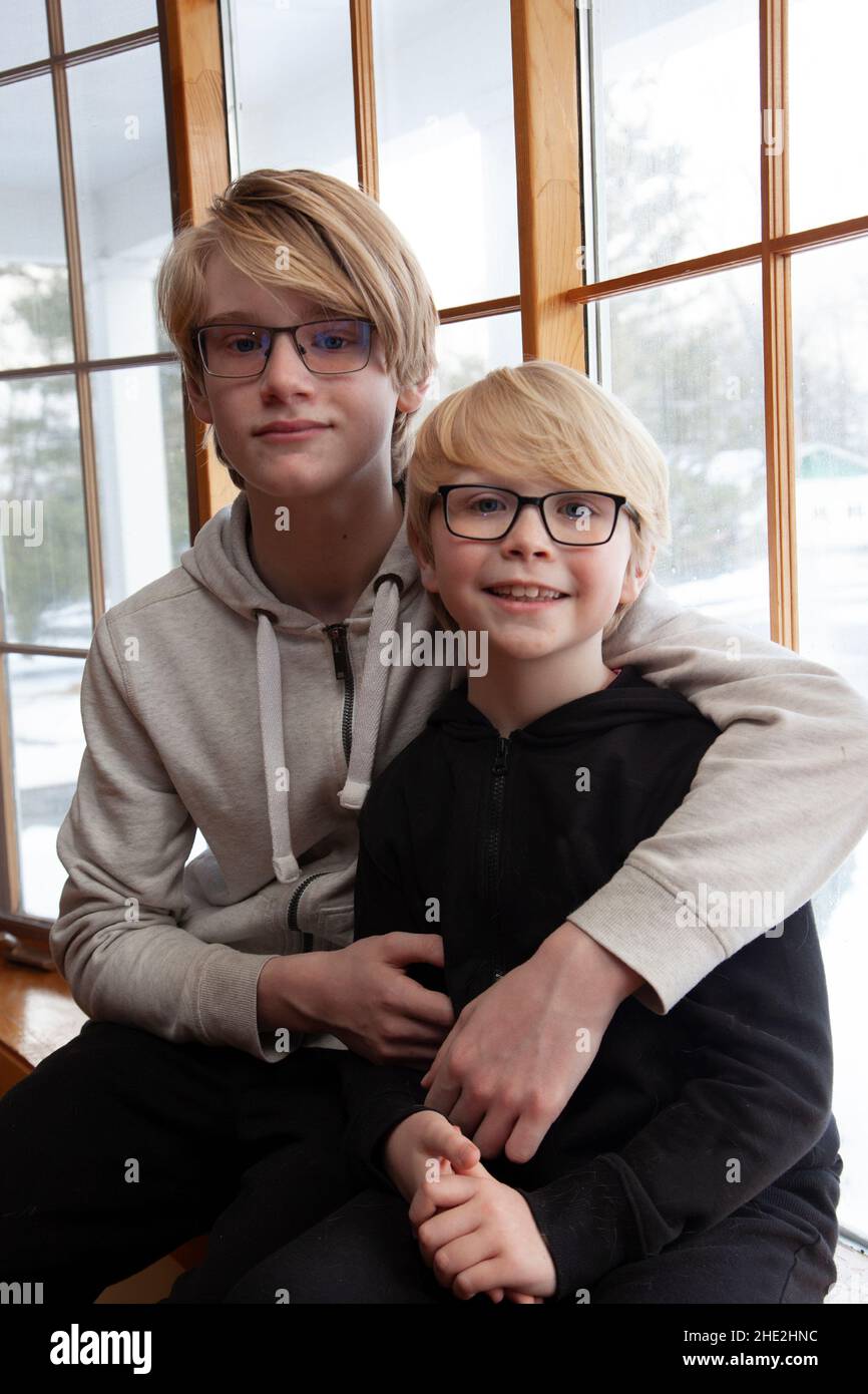 two pre-teen boys sitting together hugging affectionately in a windowsill at home Stock Photo