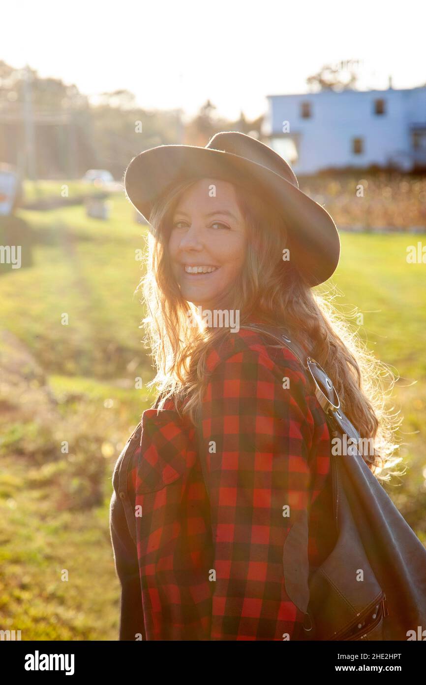 a gorgeous red haired woman wearing a hat and plaid looks back at you in the blazing sunshine Stock Photo