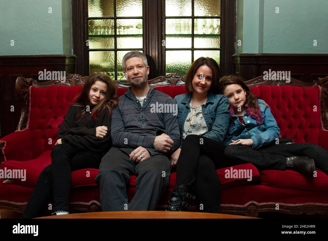 a beautiful family is very serious with a hint of smile as they relax on an elegant red couch Stock Photo