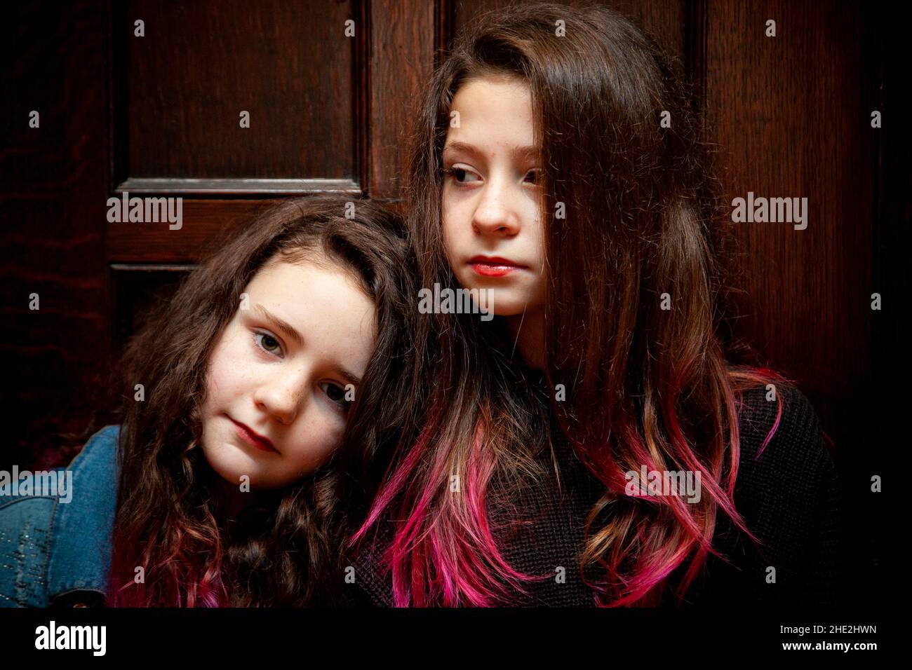 two young girls or siblings pose in a serious expression while leaning on each other Stock Photo