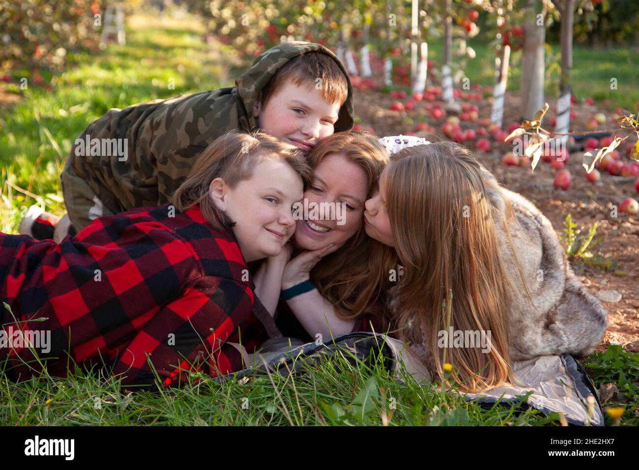 a red haired mother smiles and recieves kisses from her three freckled children Stock Photo