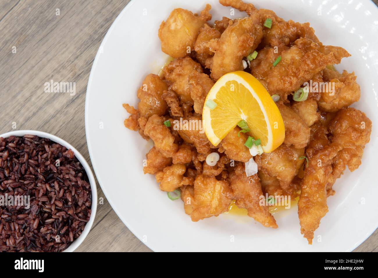 Overhead view of breaded orange chicken crispy on the outside with sliced citrus twist on top of generous pile of food. Stock Photo