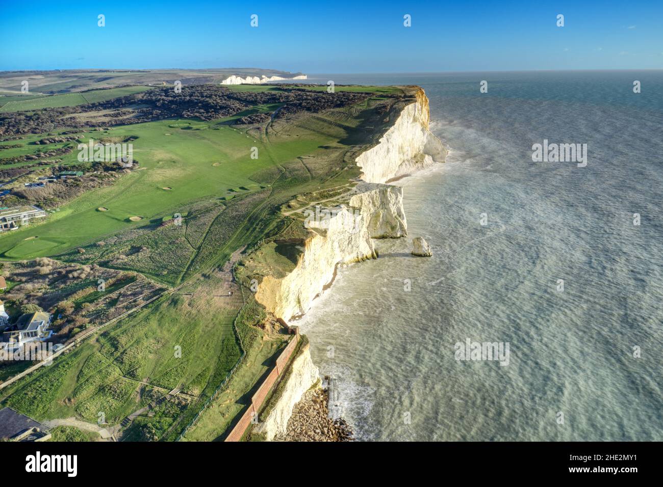 The white chalk cliffs at Seaford Head and the seven sisters in the background in East Sussex with the Golf Course in the background running along the Stock Photo