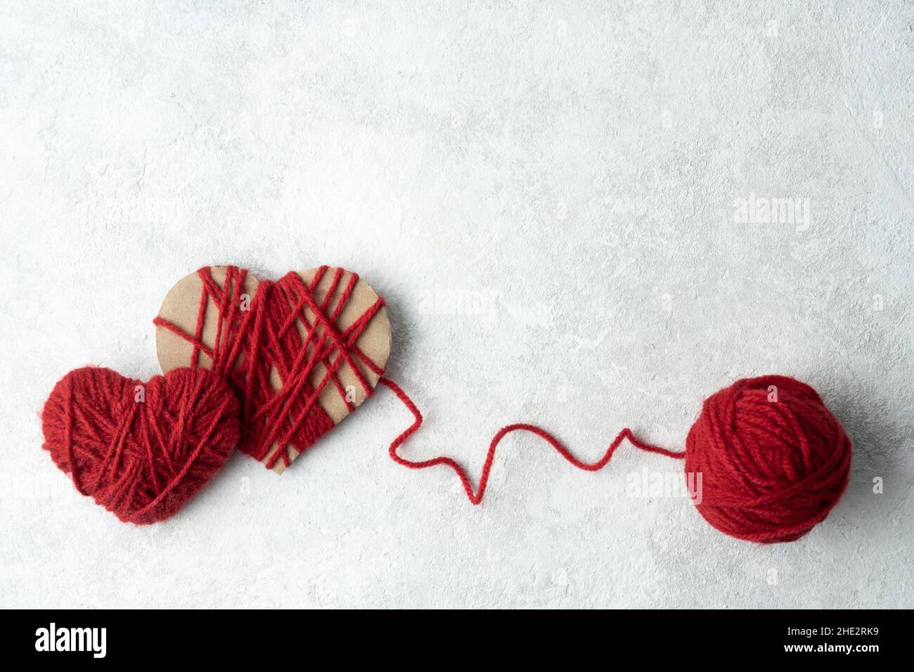 Two hearts made of red woolen yarn and a ball of thread on a white ...