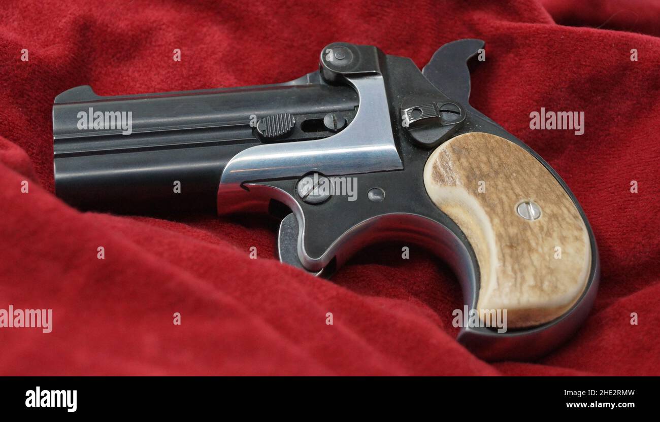 A double barrel derringer style pistol on a red velvet background. This kind of weapon was used by gamblers and women in the past because of its size Stock Photo