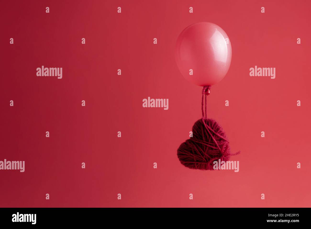 Heart of yarn flying in a balloon on a red background, Valentine's Day greeting card. Stock Photo