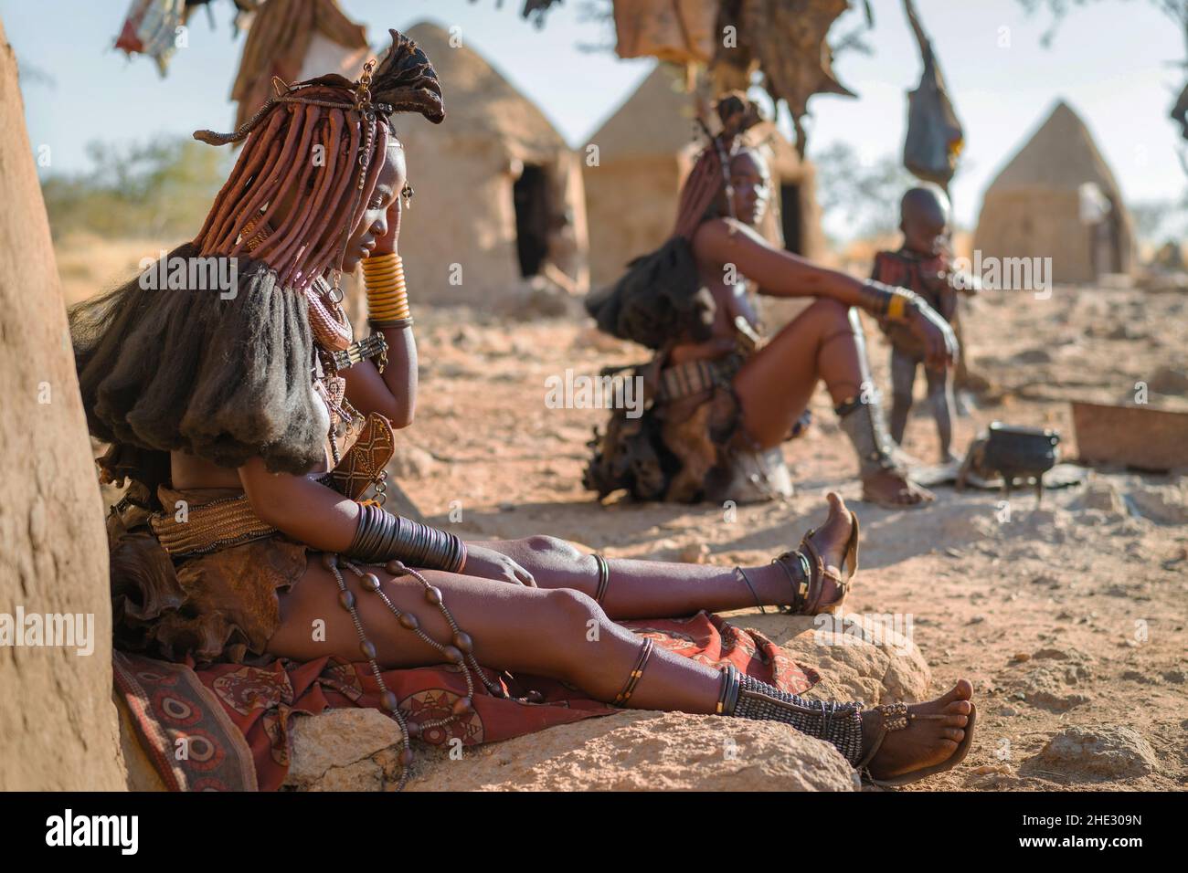 Himba women sitting outside their huts in a traditional Himba village near Kamanjab in northern Namibia, Africa. Stock Photo