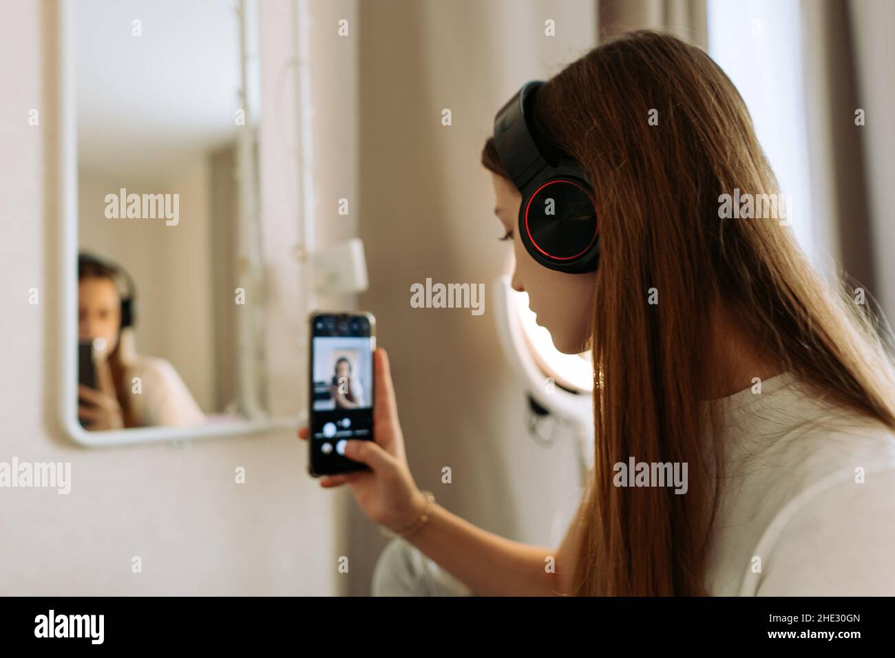 Teenage girl in headphones at mirror takes selfie, admires Stock Photo