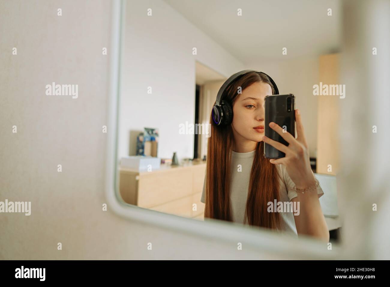 Teenage girl in headphones in front of mirror takes selfie Stock Photo