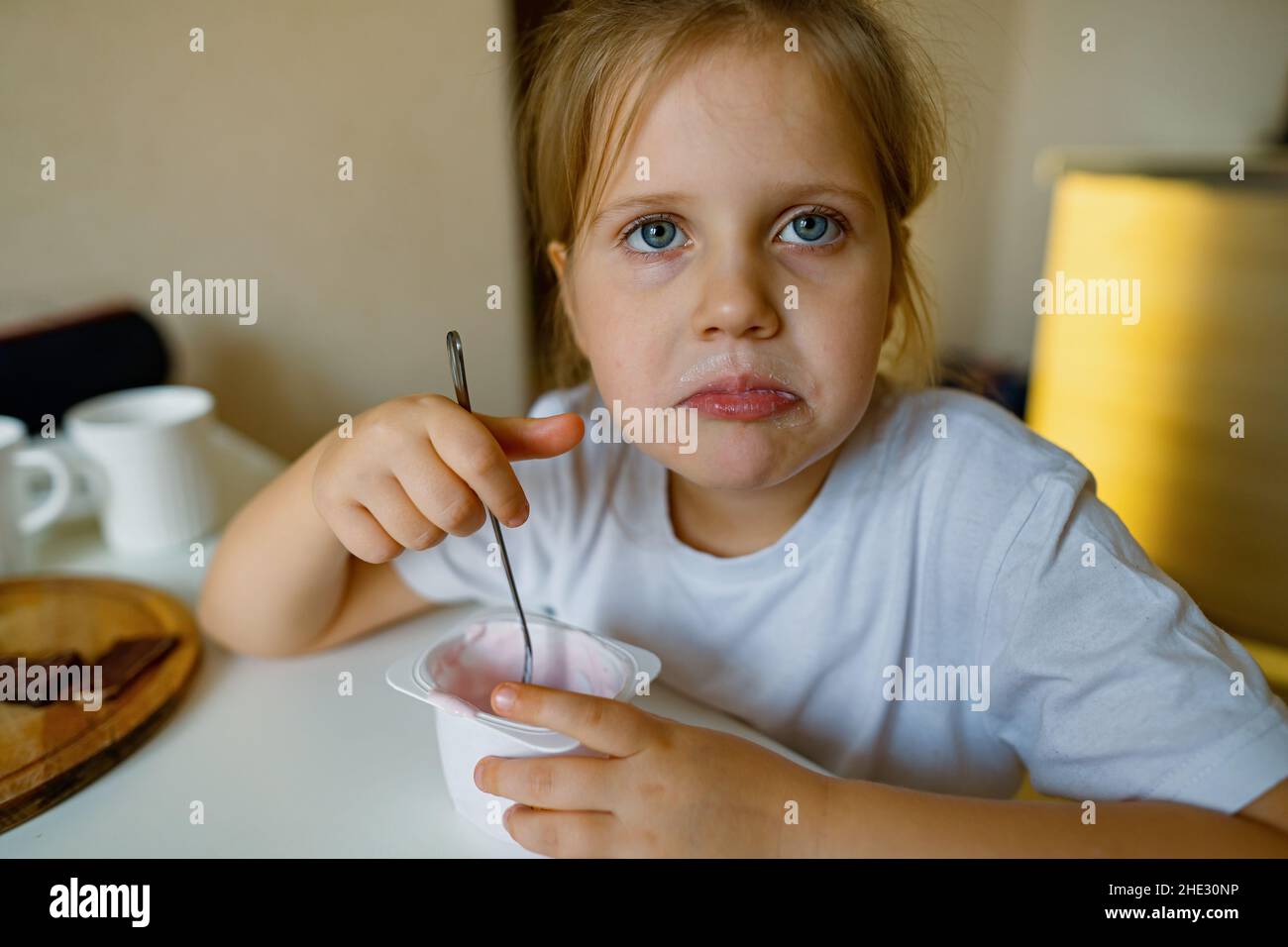 Cute girl eats yogur, has dirty mouth, has fun, grimaces Stock Photo