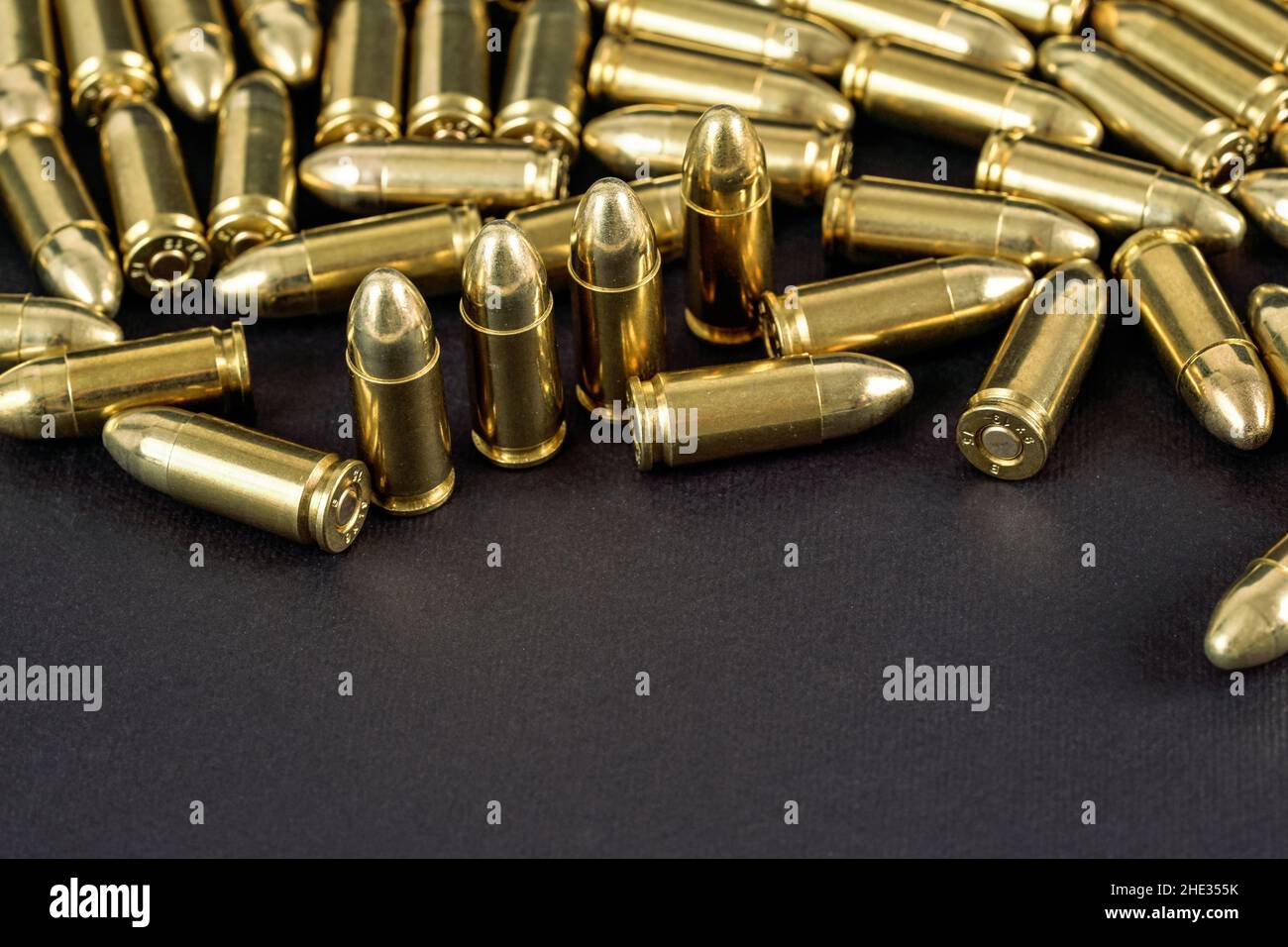 Many brass gun bullets on black table closeup view, space for text bottom part Stock Photo