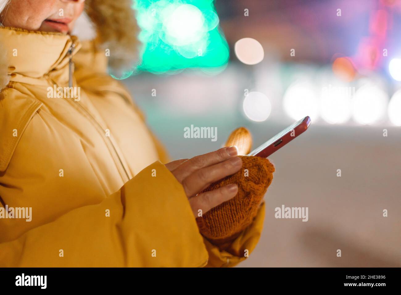 Cheerful mature 50s woman wearing warm clothes holding mobile phone in a city in winter Stock Photo