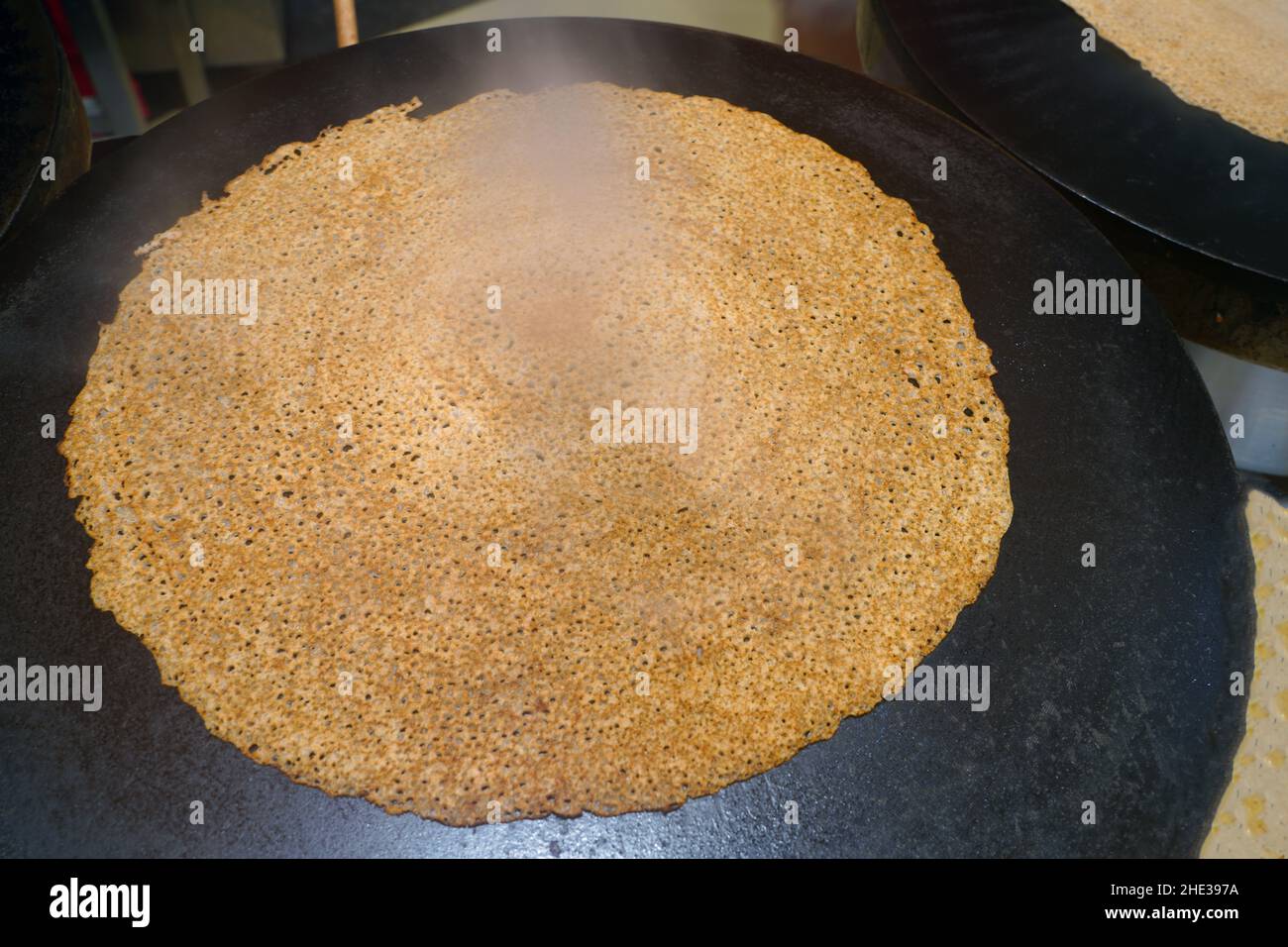 A buckwheat galette cooking on a traditional crepe griddle in Brittany, France Stock Photo