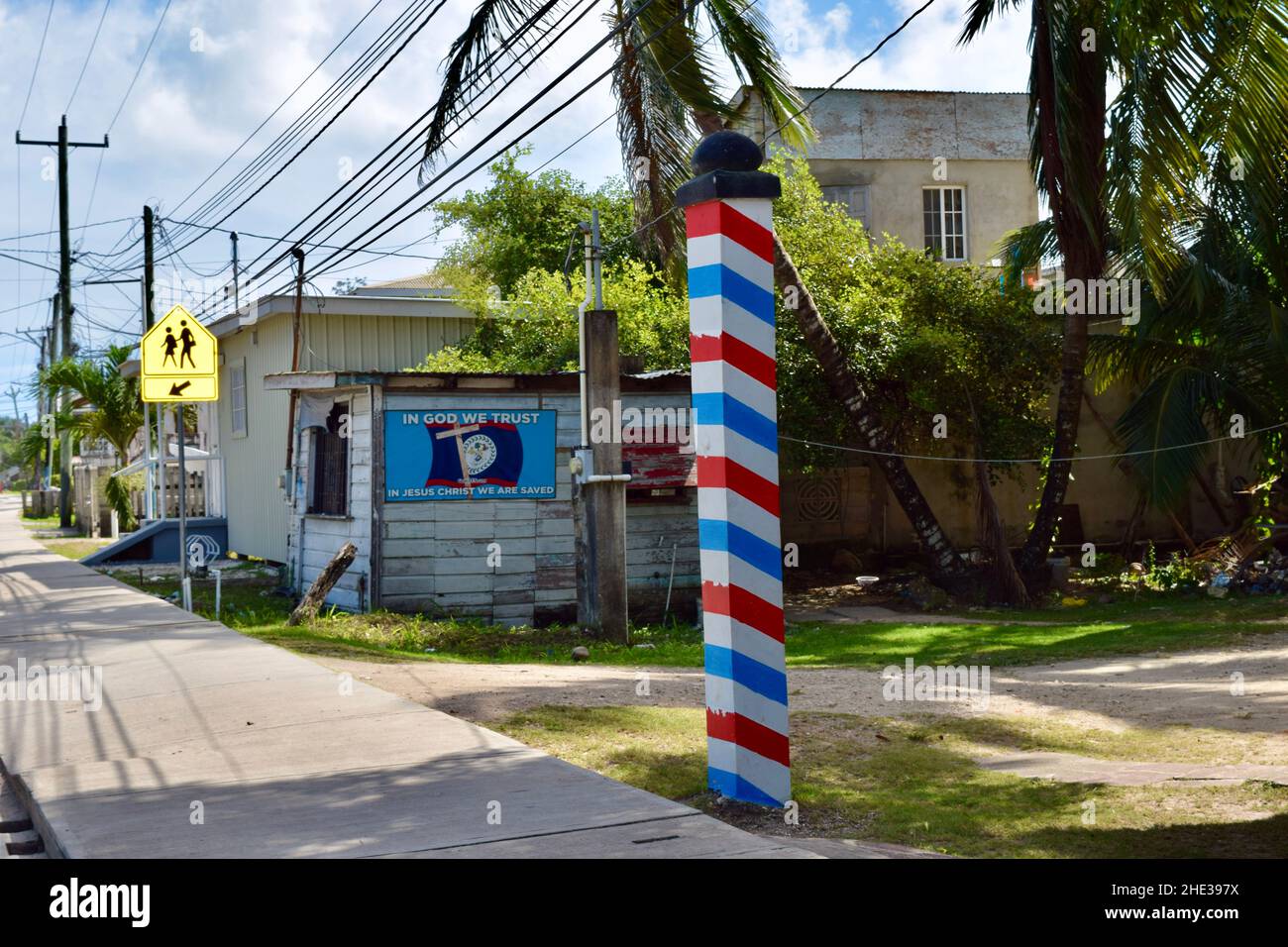 A typical neighborhood street in Belize City, Belize with a barber shop insignia, the Belizean flag, and a crosswalk sign. Stock Photo