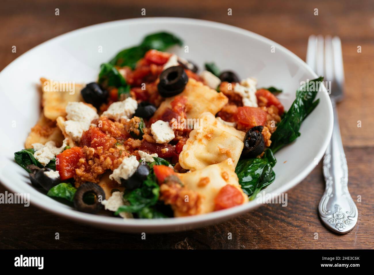 Bowl with vegan ravioli with spinach, TVP, olives, a tomato sauce and home made vegan feta. Stock Photo