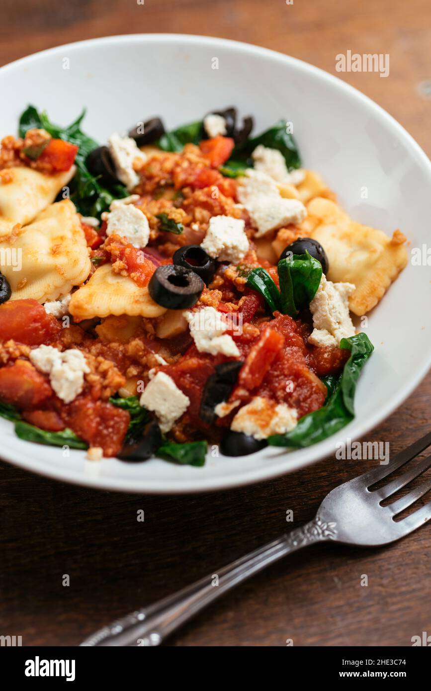 Bowl with vegan ravioli with spinach, TVP, olives, a tomato sauce and home made vegan feta. Stock Photo