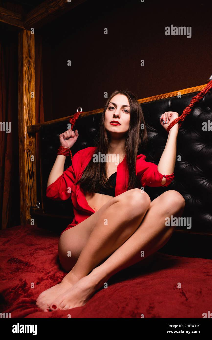 Bondage woman tied to bed with red ropes. Portrait of a young woman with tied hands to the