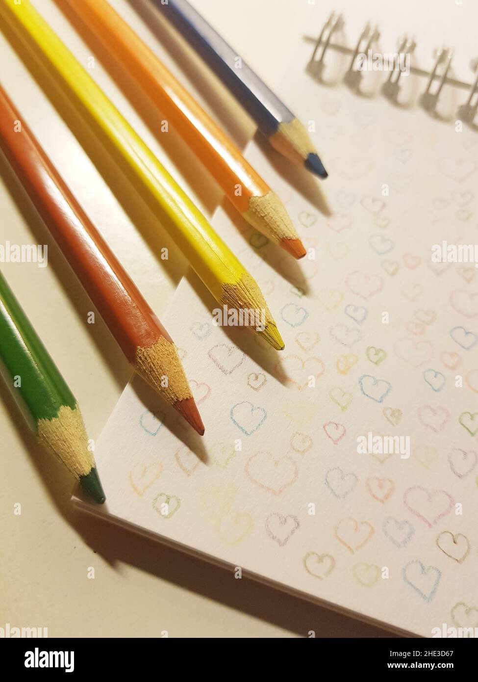 colored pencils on white notebook paper with drawn hearts. Stock Photo