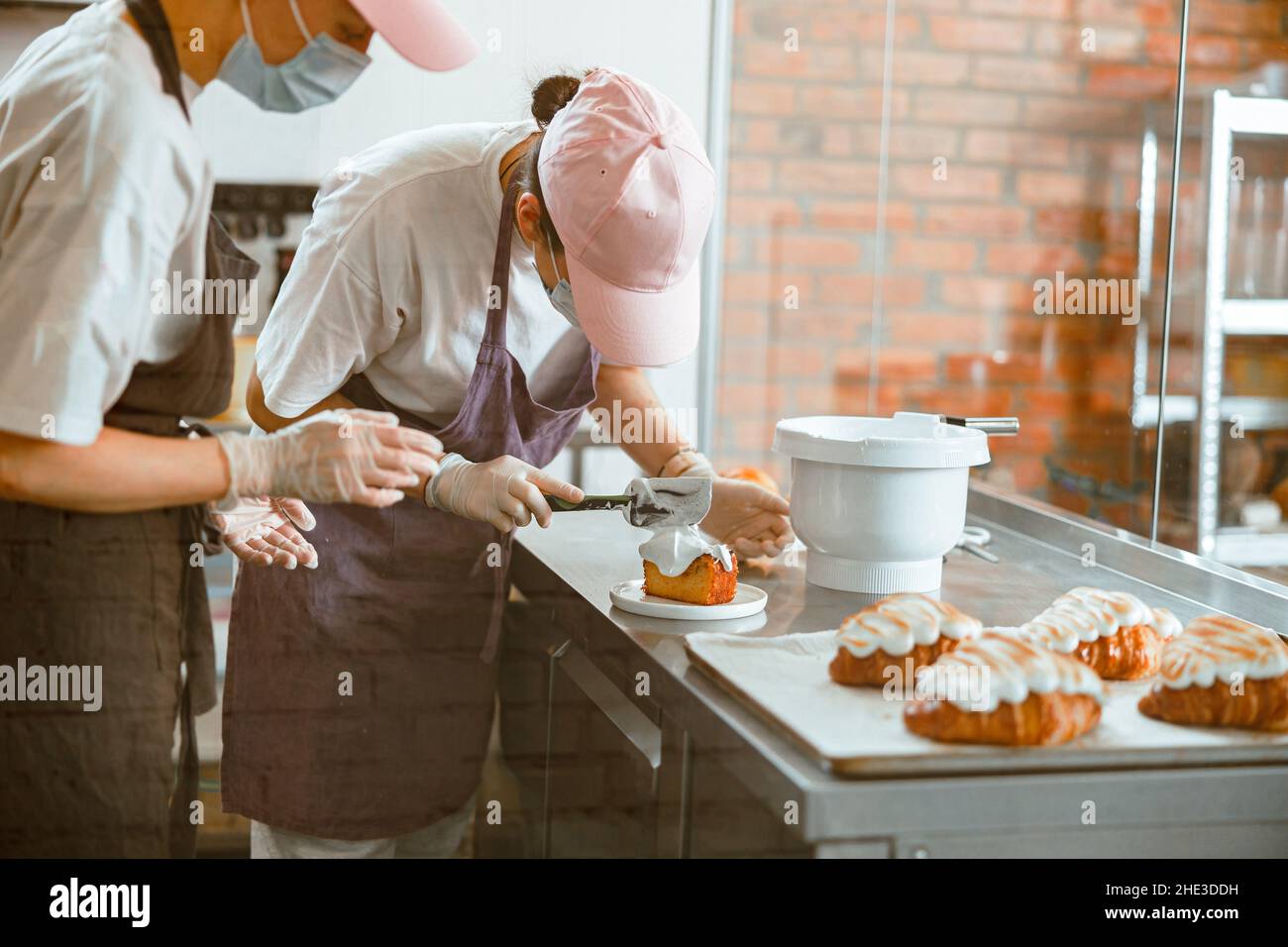 Confectioner trainee spreads cream onto sponge cake while colleague ...