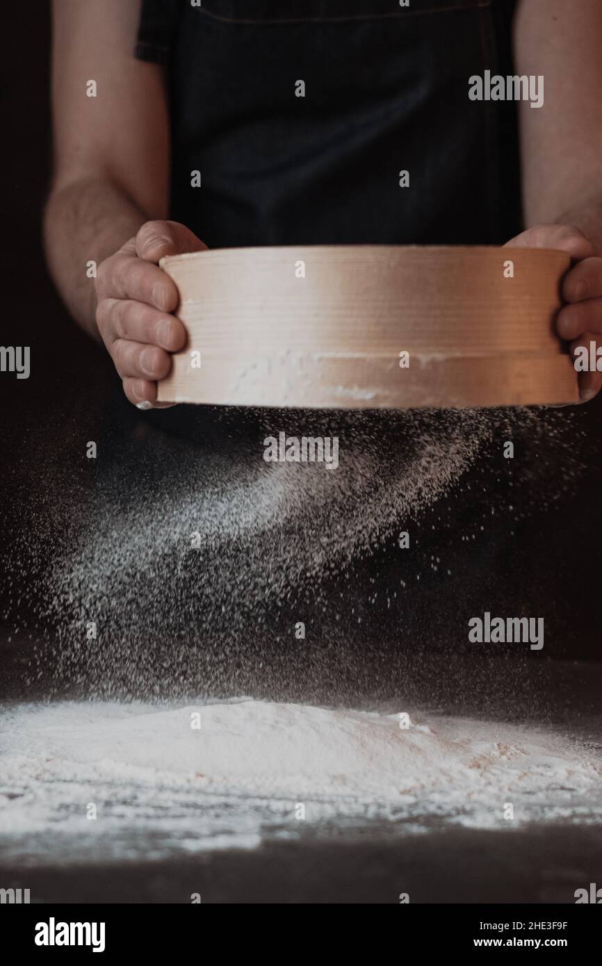 Men's hands are sifting flour through a sieve on black background Stock ...