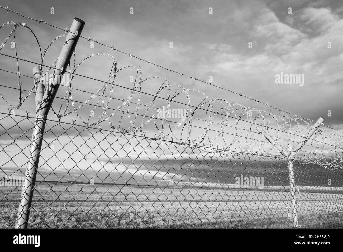 NATO barb wire with sharp and dangerous razor blades mounted on a chicken wire fence at a state border Stock Photo