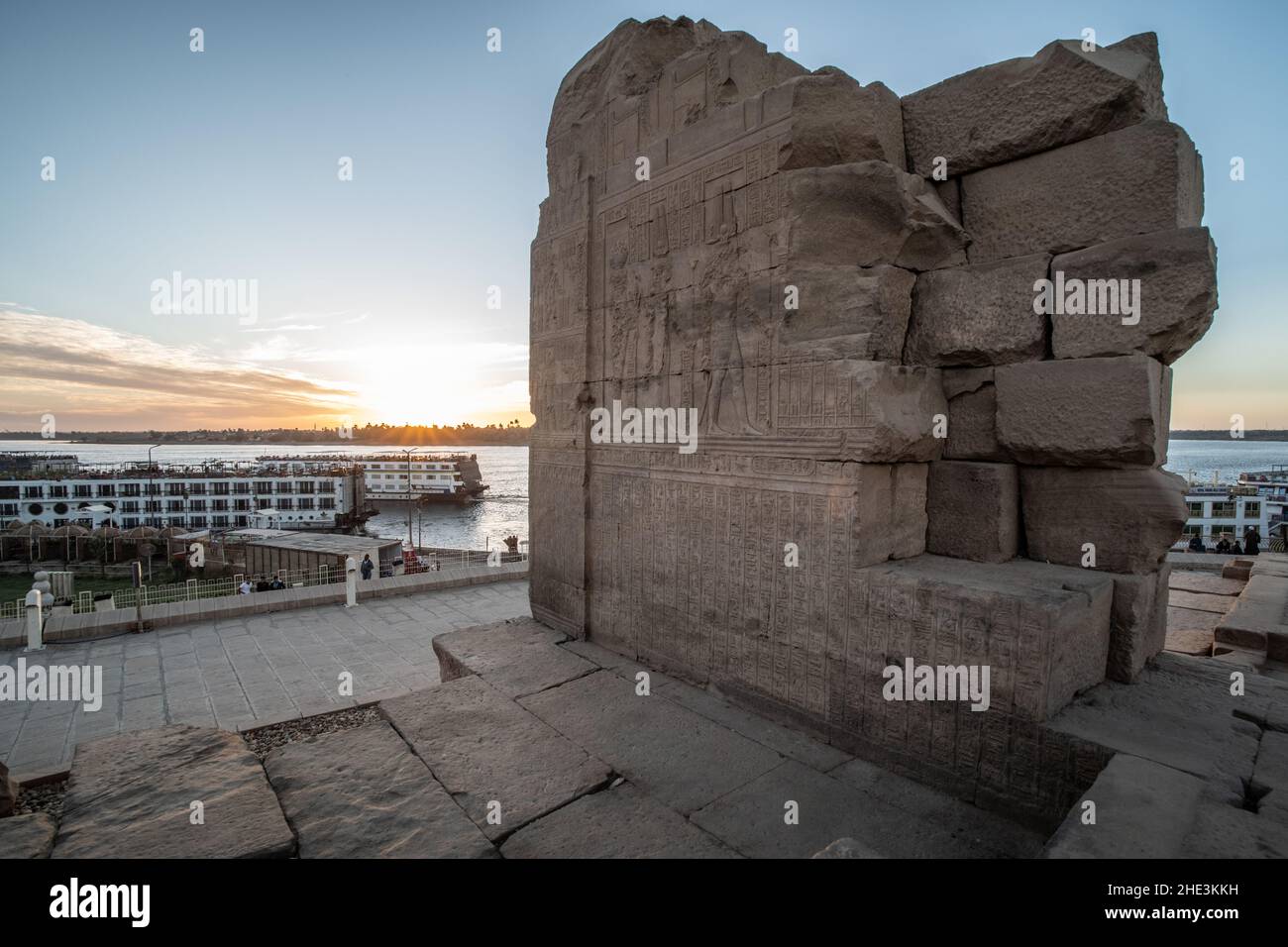 An ancient ruin at Kom Ombo temple overlooking the Nile river and docked cruise boats that bring tourists to the historic monument. Stock Photo