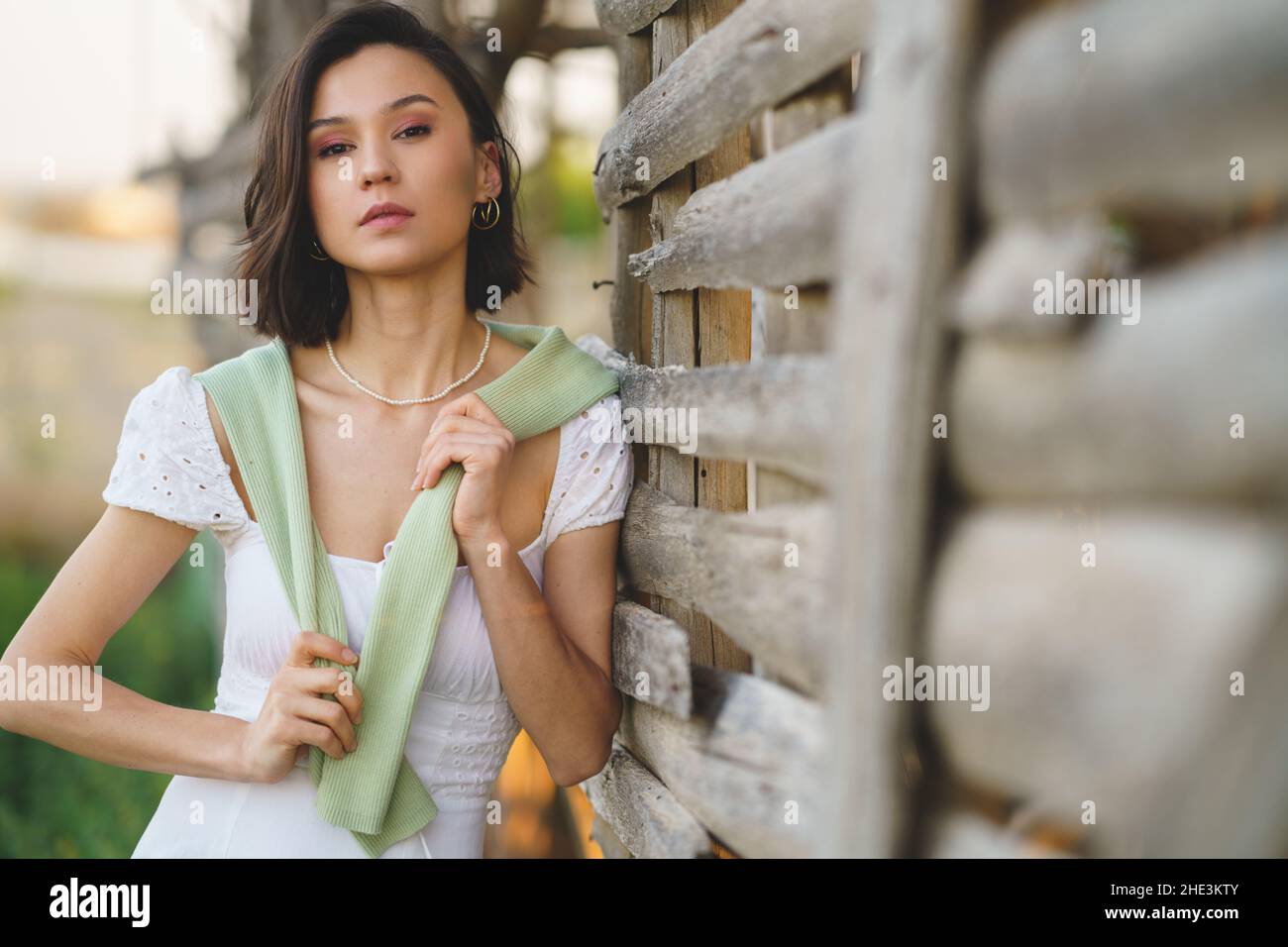 Asian woman, posing near a tobacco drying shed, wearing a white dress and green wellies. Stock Photo