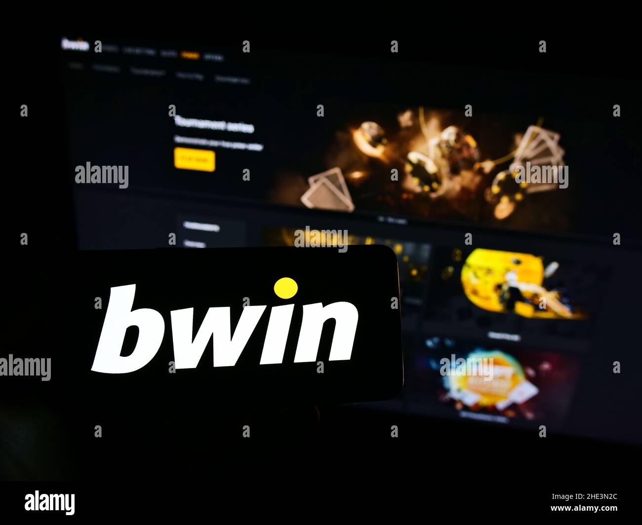 Person holding mobile phone with logo of Austrian company bwin Interactive Entertainment AG on screen in front of web page. Focus on phone display. Stock Photo