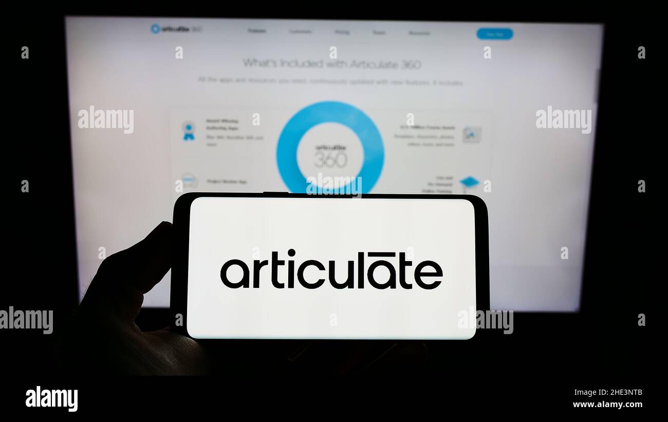 Person holding cellphone with logo of US e-learning company Articulate Global LLC on screen in front of business webpage. Focus on phone display. Stock Photo