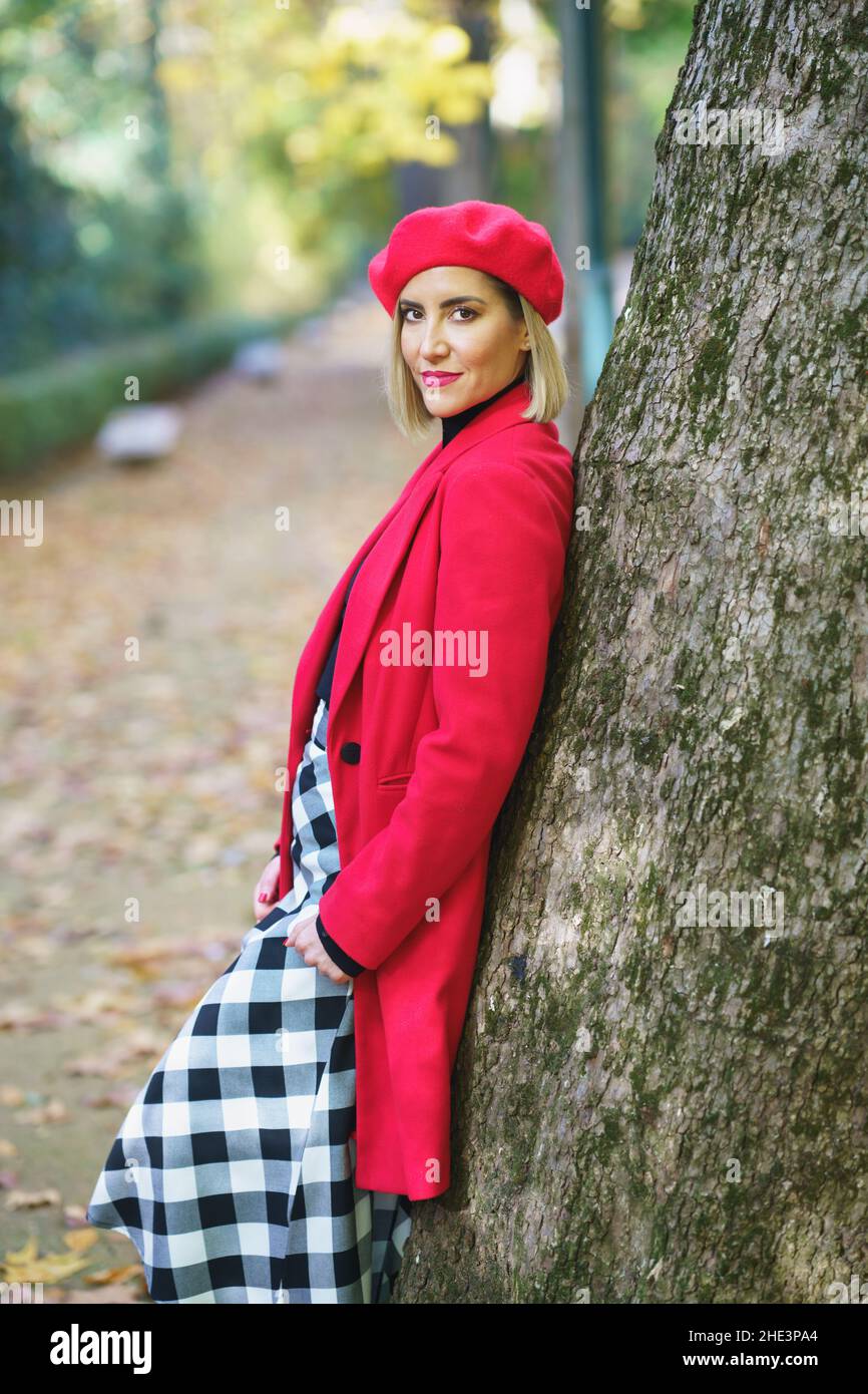 Beautiful middle-aged woman leaning on a tree trunk in a charming urban park. Stock Photo
