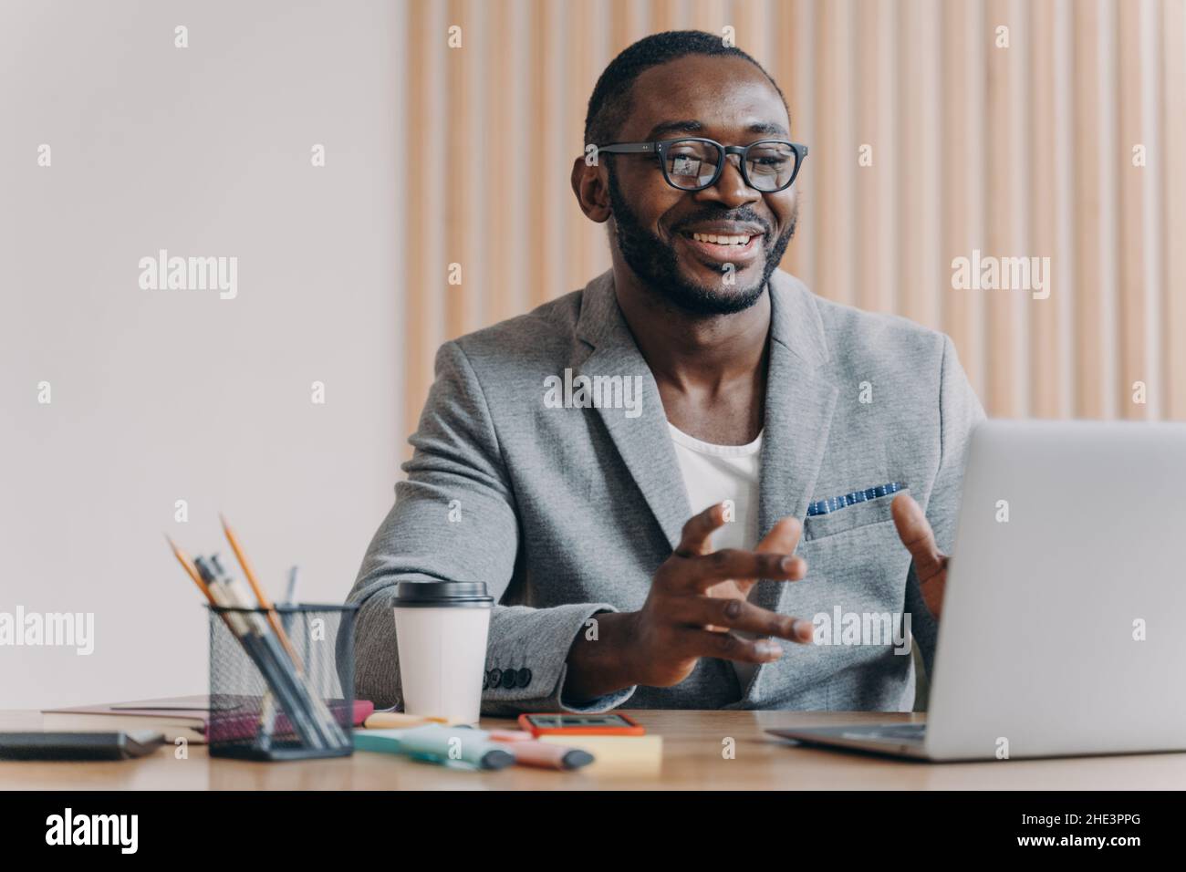 Joyful Afro american businessman wearing glasses and stylish blazer making video call on laptop Stock Photo