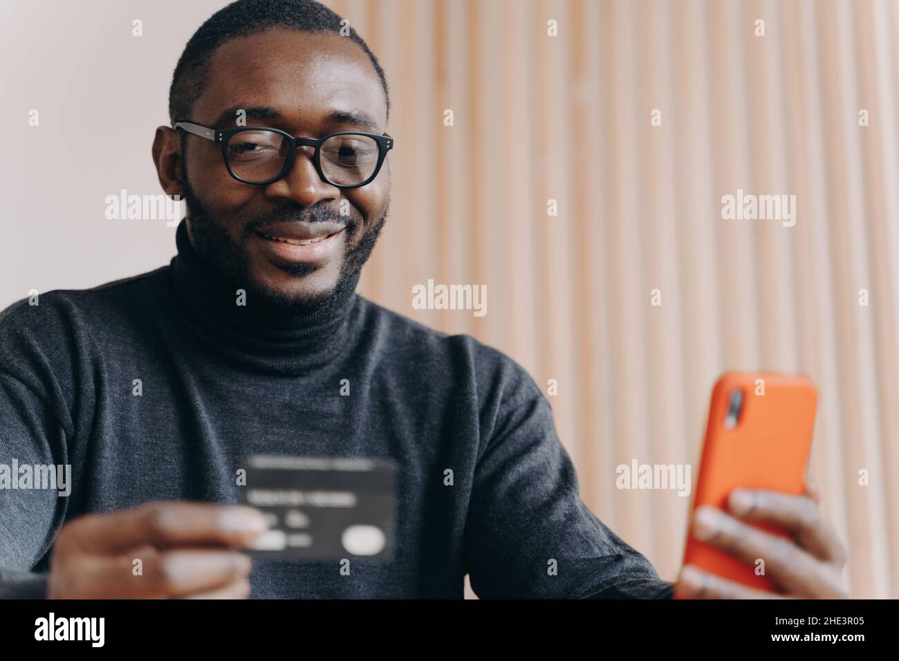 Young positive African ethnicity man entrepreneur in glasses paying with credit card online Stock Photo