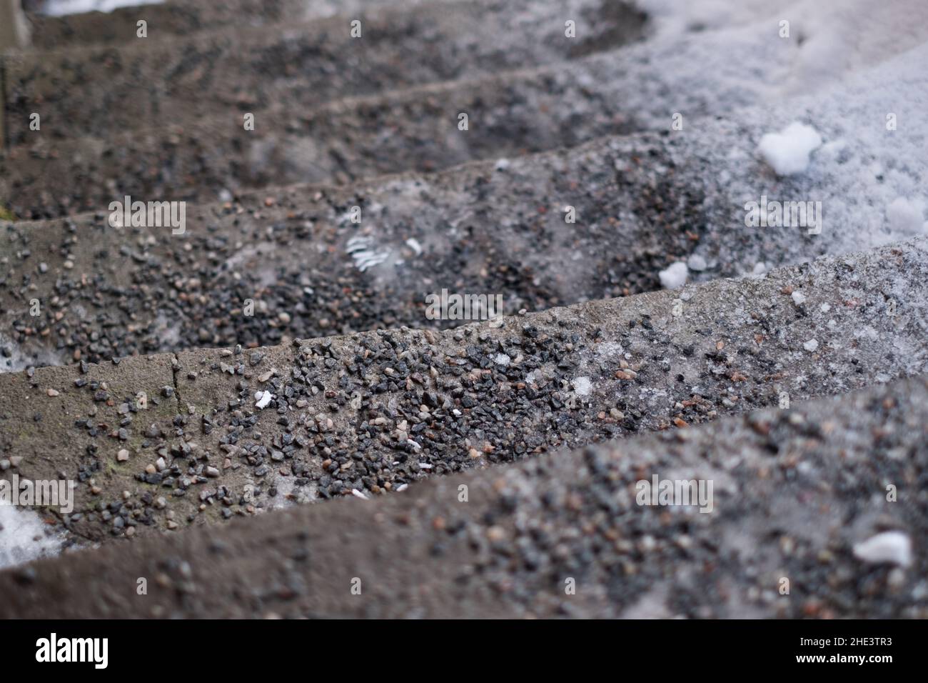 Granite rubble on icy stairs. Granite sieves sprinkled on slippery outdoor staircase steps during winter. Anti-slip maintenance. Stock Photo