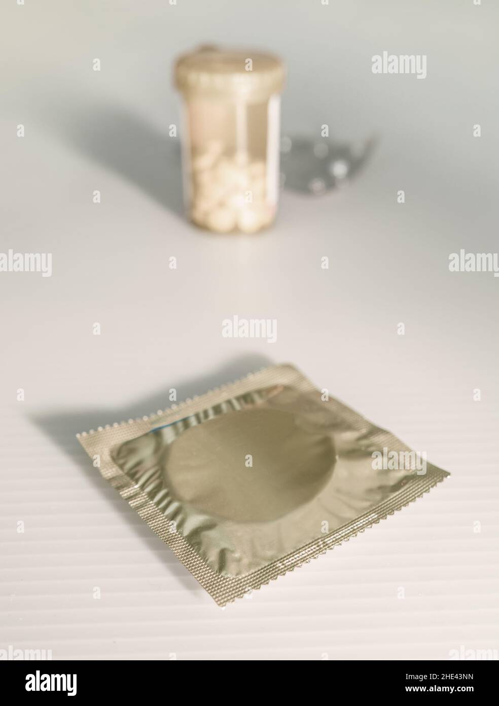 In the foreground, the condom, in the background, a container of meds and pills. Stock Photo