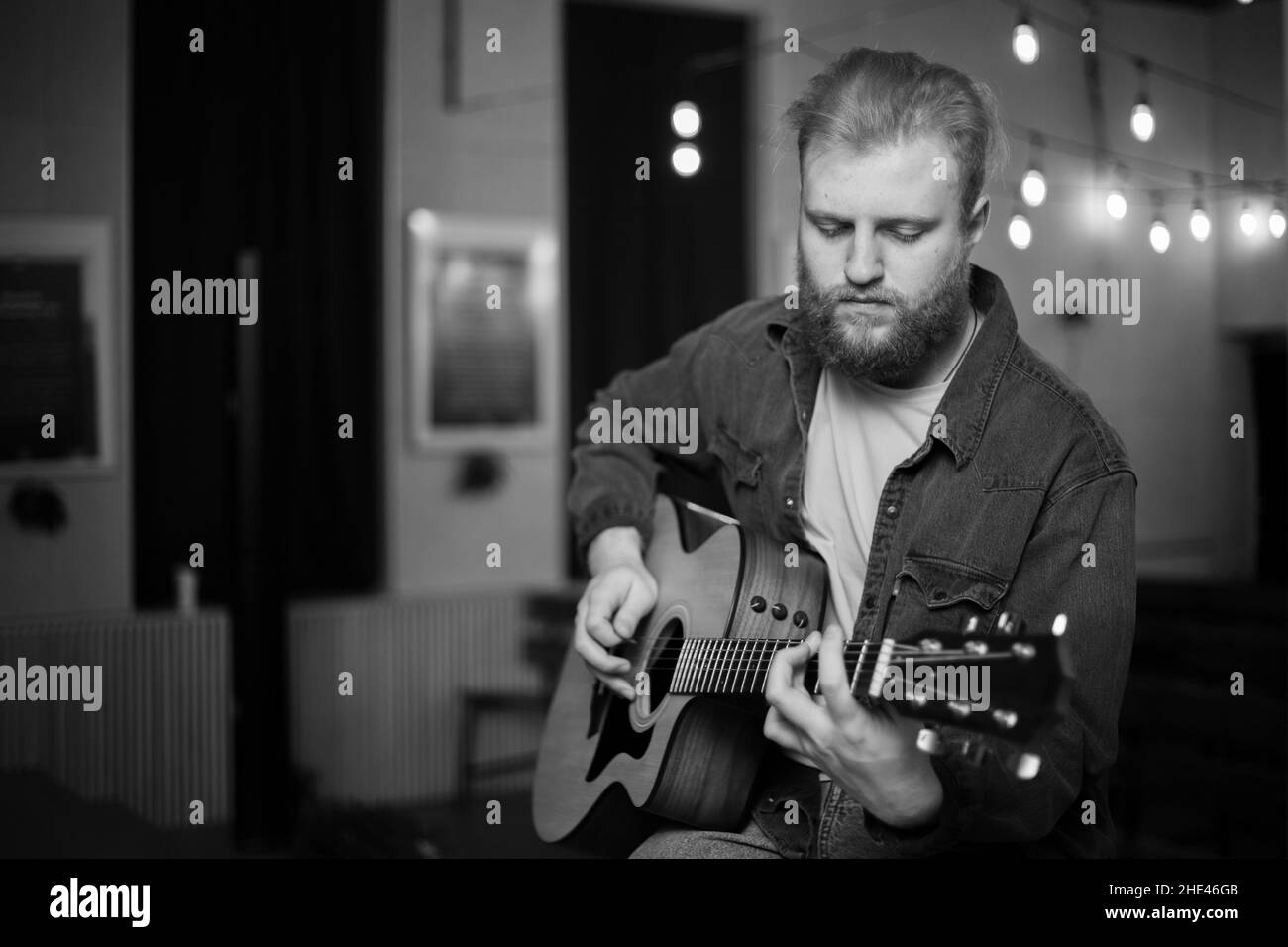 A young guy with a beard plays an acoustic guitar in a room with warm lighting Stock Photo