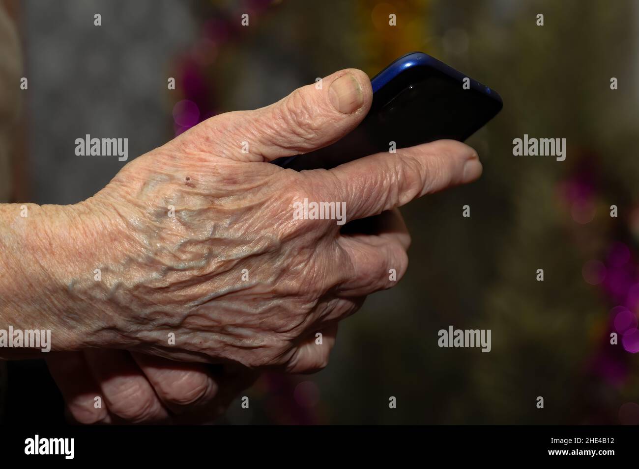 Old woman's wrinkled hand holding modern mobile phone Stock Photo